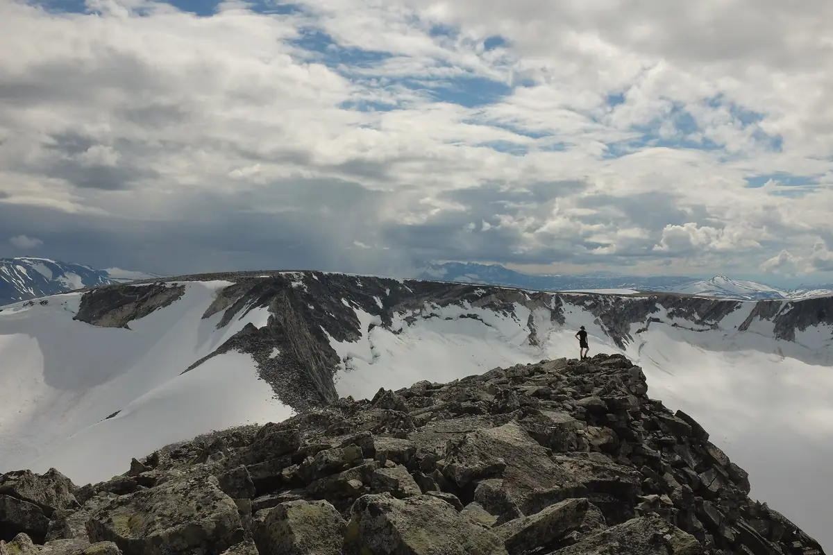 Someone on a rocky summit above snowfields in Breheimen